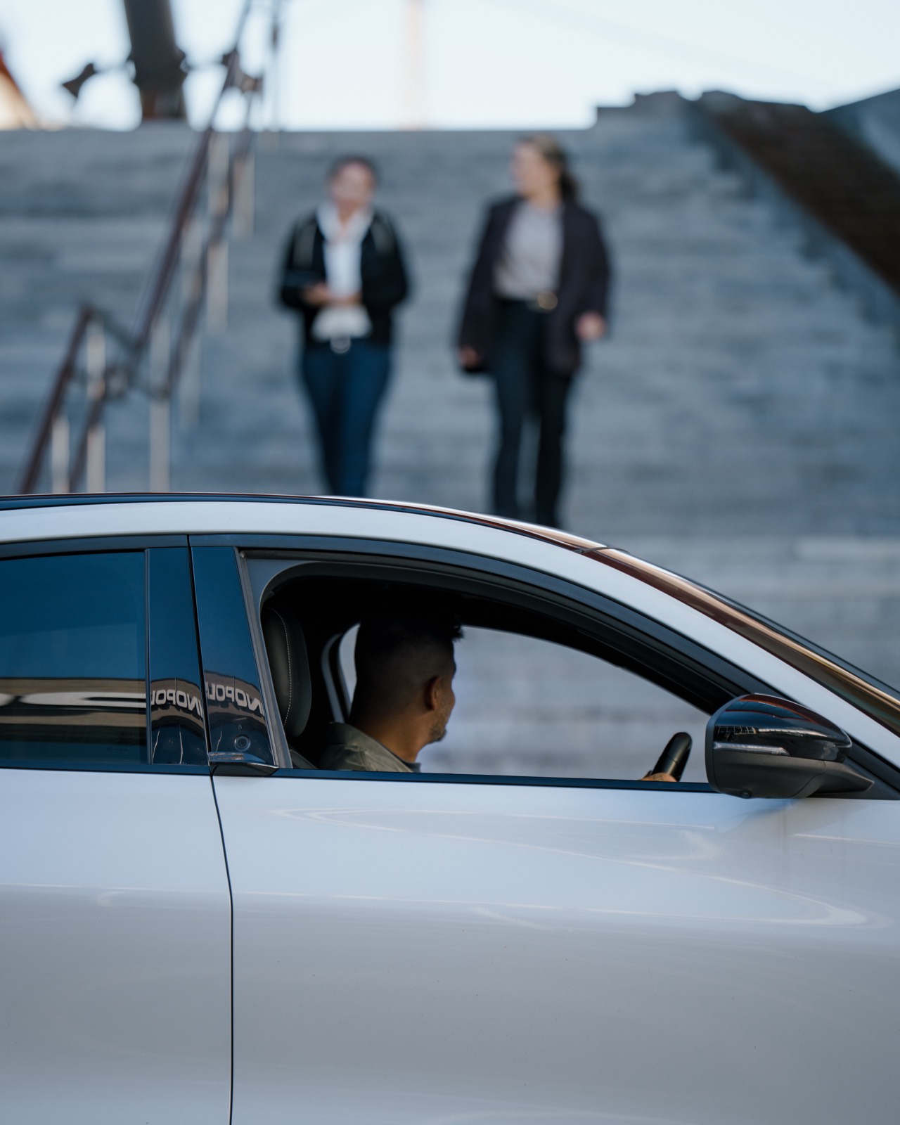 Sjåfør i hvit bil med kolleger i bakgrunn